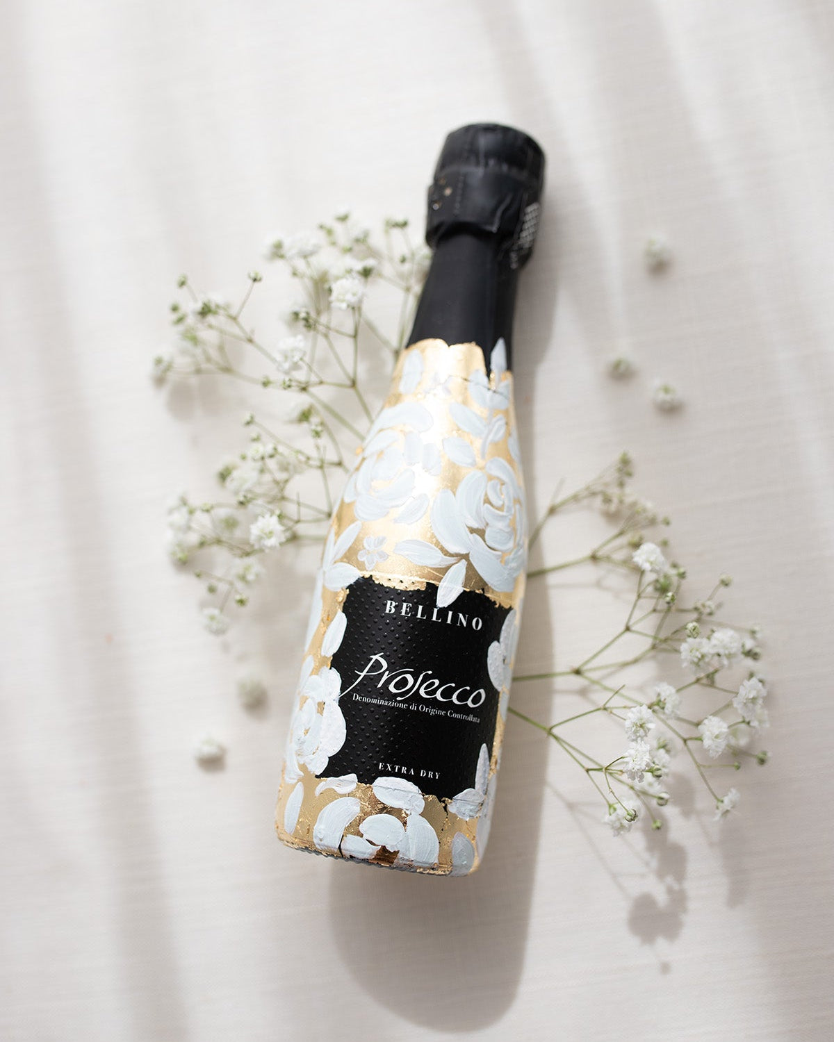 Mini bottles of Prosecco hand painted with a white roses design on a metallic gold leaf base. The perfect luxury bridesmaid proposal gift. Fancy Folk Design