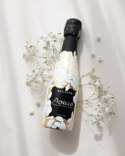 Mini bottles of Prosecco hand painted with a white roses design on a metallic gold leaf base. The perfect luxury bridesmaid proposal gift. Fancy Folk Design
