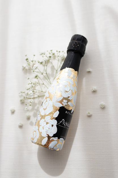 Mini bottles of Prosecco hand painted with a white roses design on a metallic gold leaf base. The perfect luxury bridesmaid proposal gift. Fancy Folk Design