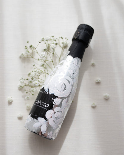 Mini bottles of Prosecco hand painted with a white roses design on a metallic silver leaf base. The perfect luxury bridesmaid proposal gift. Fancy Folk Design