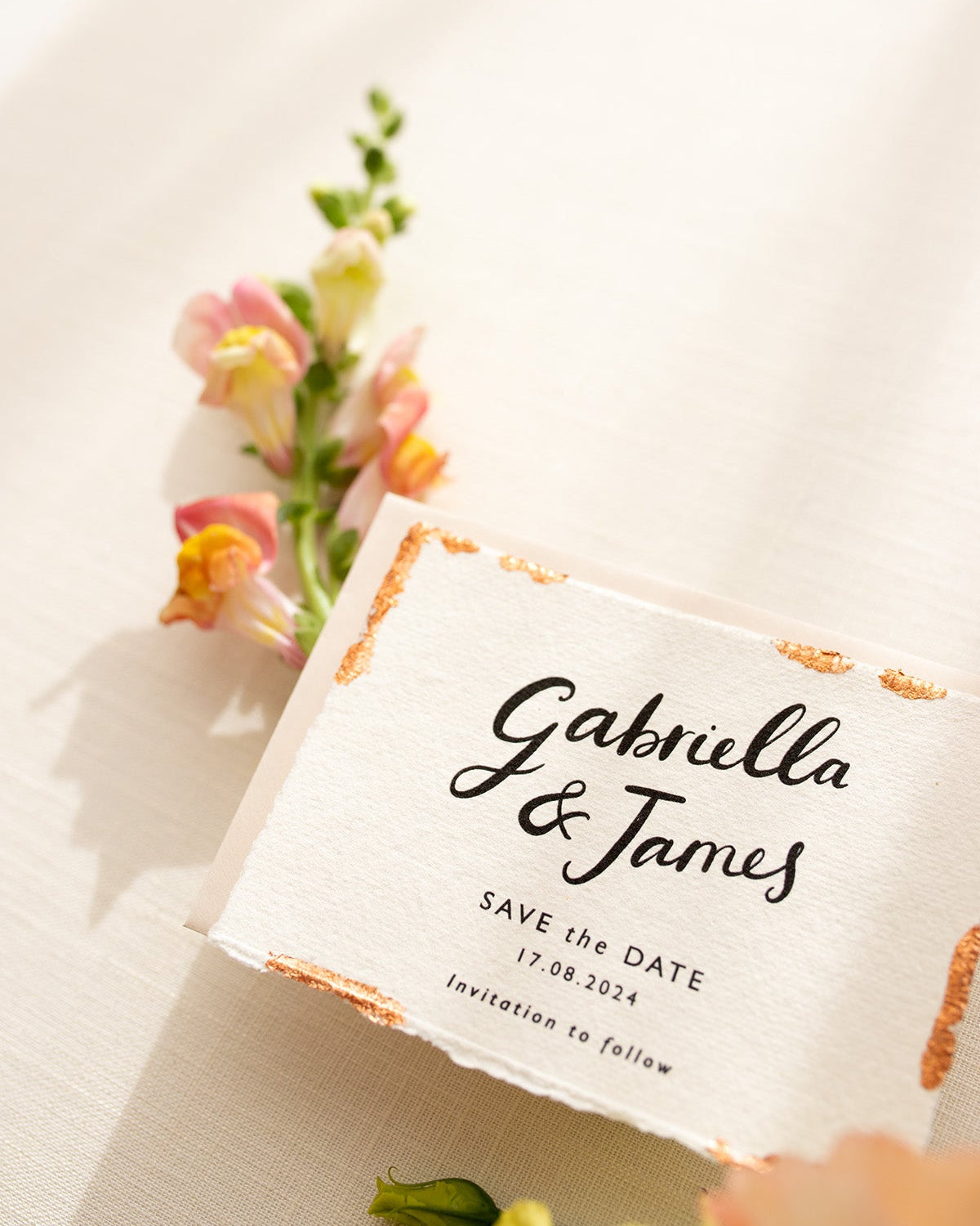 Wedding Save The Date. Beautiful calligraphy names read"Gabriella & James" with  wedding date below. Printed onto tactile Indian handmade cotton paper. The cards have hand torn edges for a romantic feel with copper leaf accents which sparkle.  Paired with a neutral almond coloured envelope. Fancy Folk