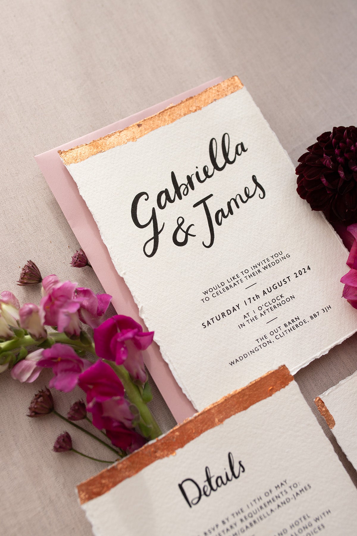 Modern Calligraphy Wedding Invitation,  with blush pink coloured envelopes. Our wedding stationery features a beautiful hand lettered calligraphy names design printed on textured handmade Indian paper, with hand torn edges for a soft romantic feel. Each piece is lovingly hand finished with copper leaf for a luxury feel. Styled with burgundy and pink florals. Fancy Folk