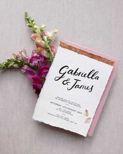Modern Calligraphy Wedding Invitation,  with blush pink coloured envelopes. Our wedding stationery features a beautiful hand lettered calligraphy names design printed on textured handmade Indian paper, with hand torn edges for a soft romantic feel. Each piece is lovingly hand finished with copper leaf for a luxury feel. Styled with burgundy and pink florals. Fancy Folk