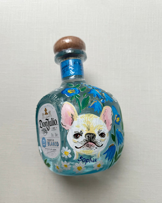 Hand painted pet portrait of a cute french bulldog on a celebration bottle of   alcohol. A pale blue bottle is decorated with beautiful blue florals and calligraphy pets name. Finished with accents of gold leaf. Perfect personalised gift. Fancy Folk
