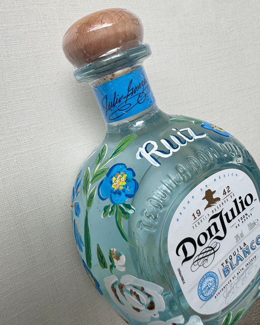 Hand painted pet portrait of a cute french bulldog on a celebration bottle of   alcohol. A pale blue bottle is decorated with beautiful blue florals and calligraphy pets name. Finished with accents of gold leaf. Perfect personalised gift. Fancy Folk