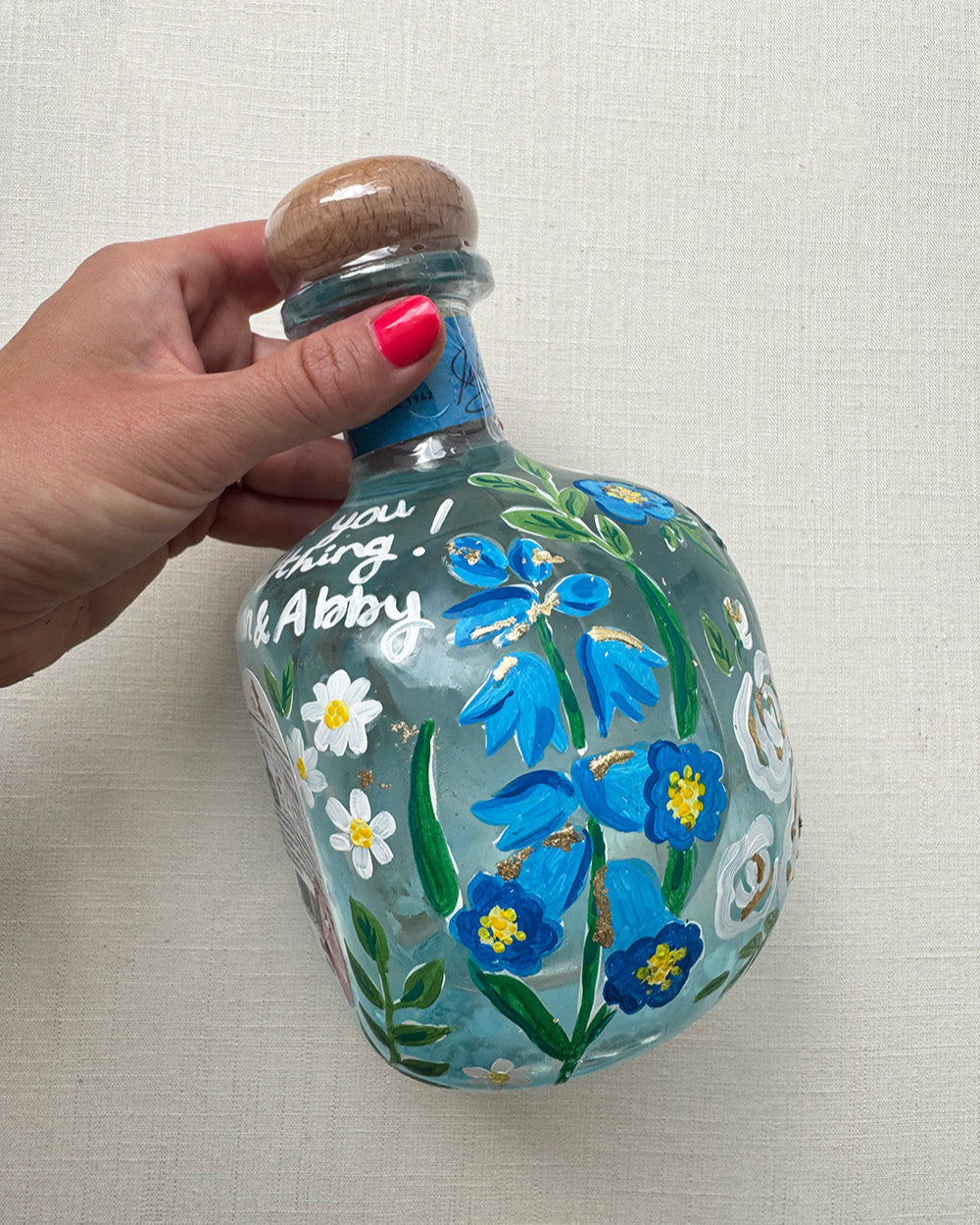 Hand painted pet portrait of a cute french bulldog on a celebration bottle of   alcohol. A pale blue bottle is decorated with beautiful blue florals and calligraphy pets name. Finished with accents of gold leaf. Perfect personalised gift. Fancy Folk