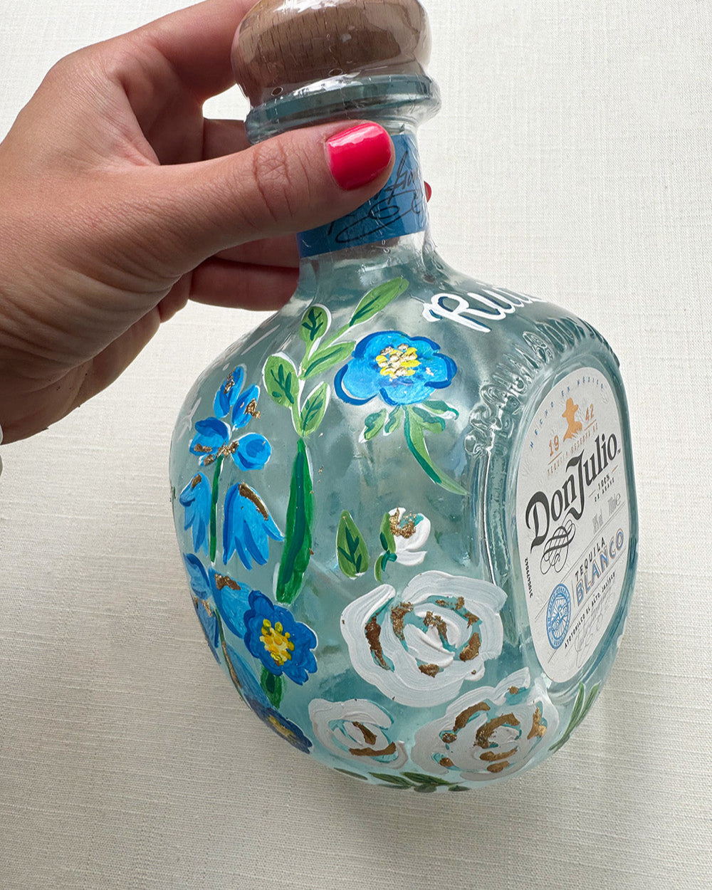 Hand painted pet portrait of a cute french bulldog on a celebration bottle of   alcohol. A pale blue bottle is decorated with beautiful blue florals and calligraphy pets name. Finished with accents of gold leaf. Perfect personalised gift. Fancy Folk