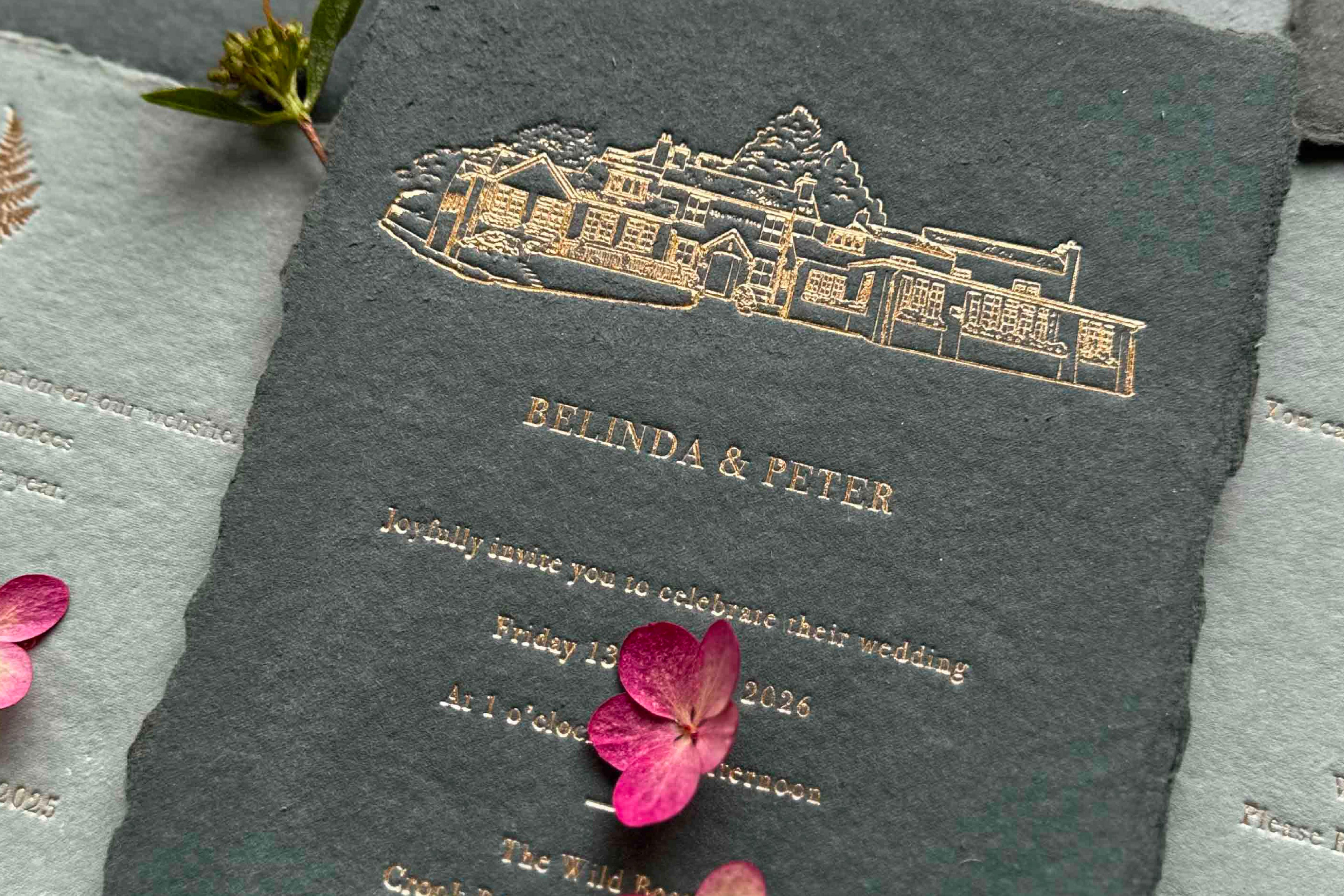 Wedding invitation card with gold foil venue illustration and text. On handmade textured paper with romantic torn edges.