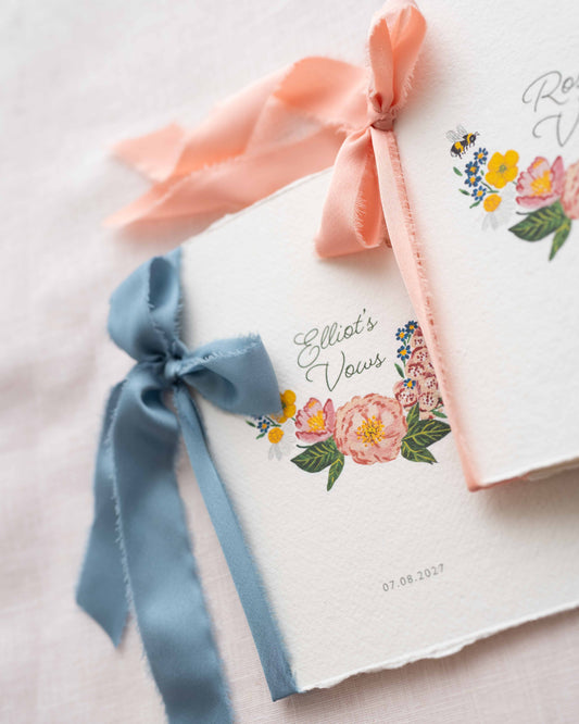 Wild flower Vow books. Watercolour hand painted florals of meadow flowers and a little bee make up a posy. Couples names are nestled in the floral with wedding date set below. Printed on handmade Indian cotton paper and styled with silk ribbon. Fancy Folk Design