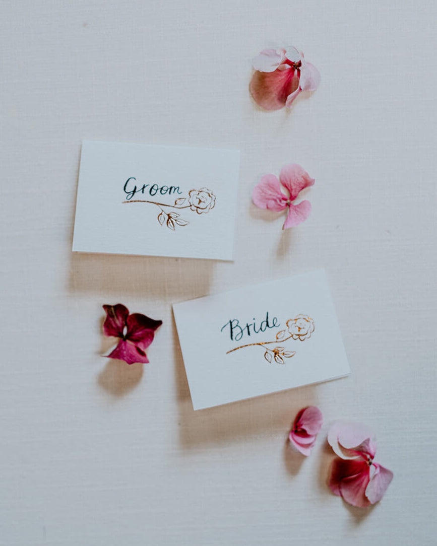 Foiled rose design place card for your wedding table with hand calligraphy bride and  groom text. Rose Gold hot foil on textured card.  Deigned by Fancy Folk wedding stationery.