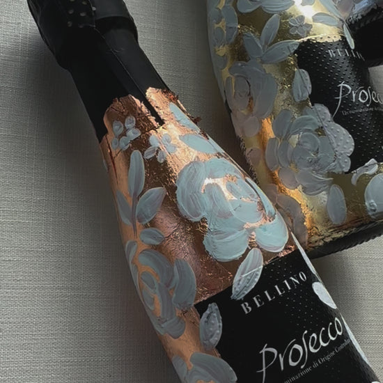 Mini bottles of Prosecco hand painted with a white roses design on a metallic base. Gold, silver and copper examples of the same design. The perfect luxury bridesmaid proposal gift. Fancy Folk Design