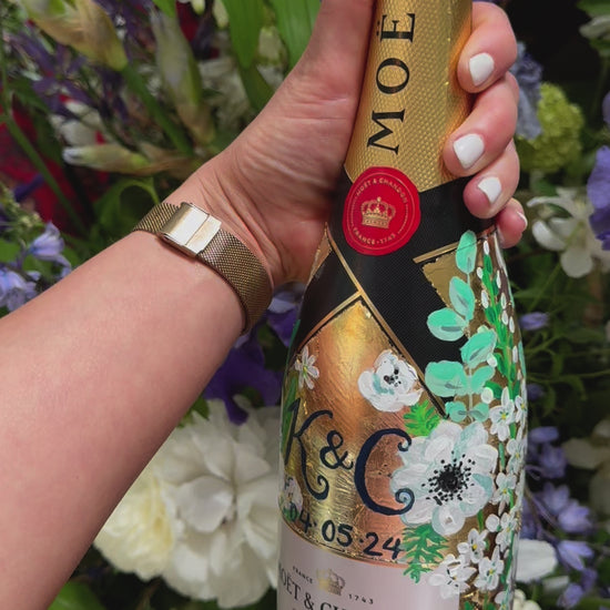 Hand painted Bottle of Moet Champagne. Perfect wedding gift with couples monogram initials and wedding date. Gold leaf base painted florals to match the bridal bouquet. Woman's hands holding the bottle. Fancy Folk Design