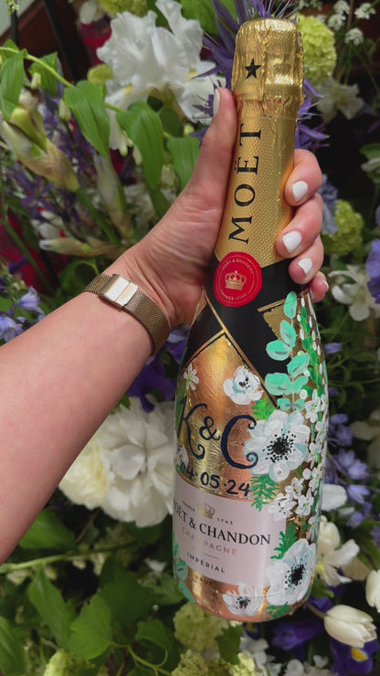 Hand painted Bottle of Moet Champagne. Perfect wedding gift with couples monogram initials and wedding date. Gold leaf base painted florals to match the bridal bouquet. Woman's hands holding the bottle. Fancy Folk Design