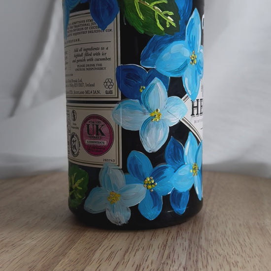 Hand painted Occasion Bottle. Blue Hydrangeas in different shades are painted all around the bottle. Calligraphy name of the recipient at the front of the bottle in white. Gold leaf accents to finish. Fancy Folk Design