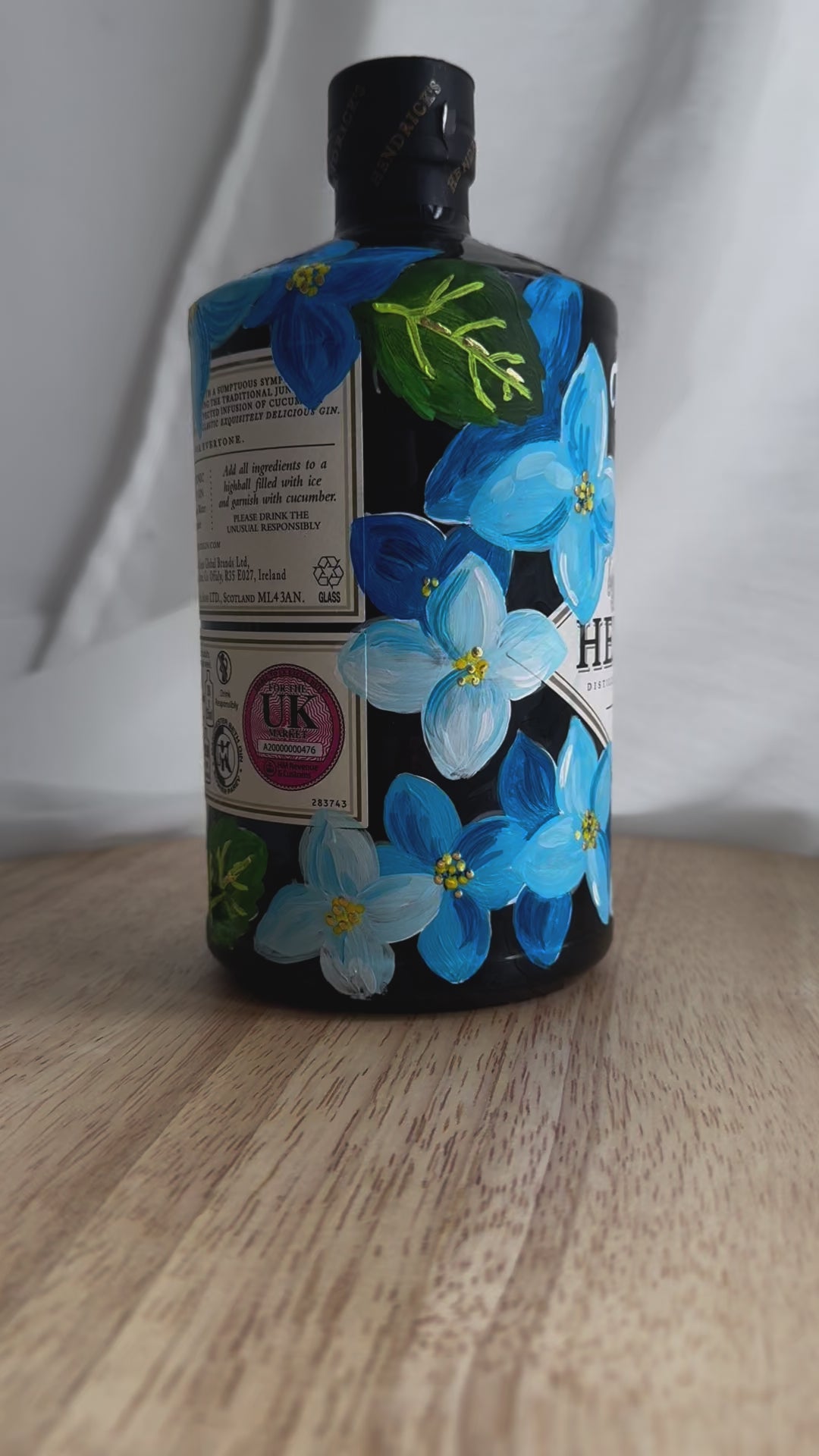 Hand painted Occasion Bottle. Blue Hydrangeas in different shades are painted all around the bottle. Calligraphy name of the recipient at the front of the bottle in white. Gold leaf accents to finish. Fancy Folk Design