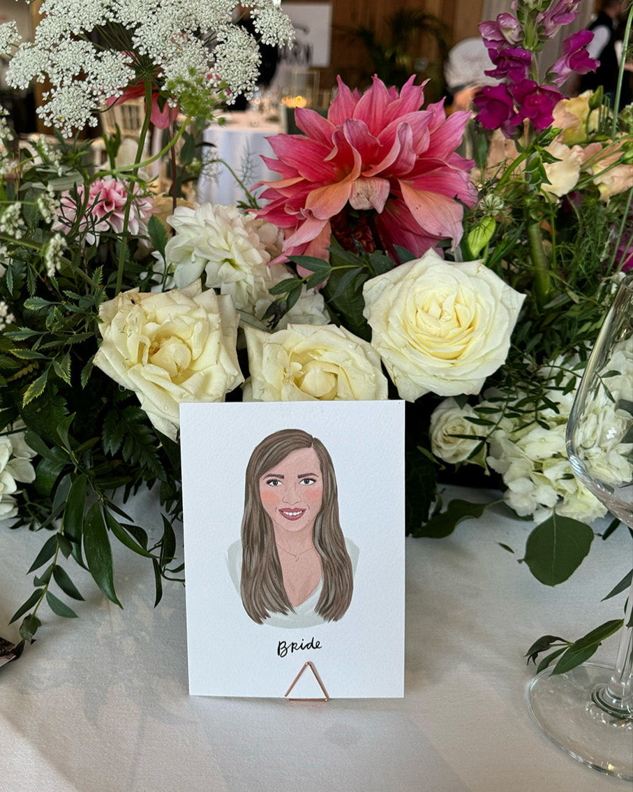Illustrated wedding portrait of the bride used as a table place card. Surrounded by florals. Fancy Folk.