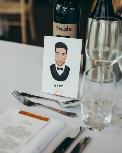 Illustrated wedding portrait of the groom used as a table place card. Surrounded by florals. Fancy Folk.